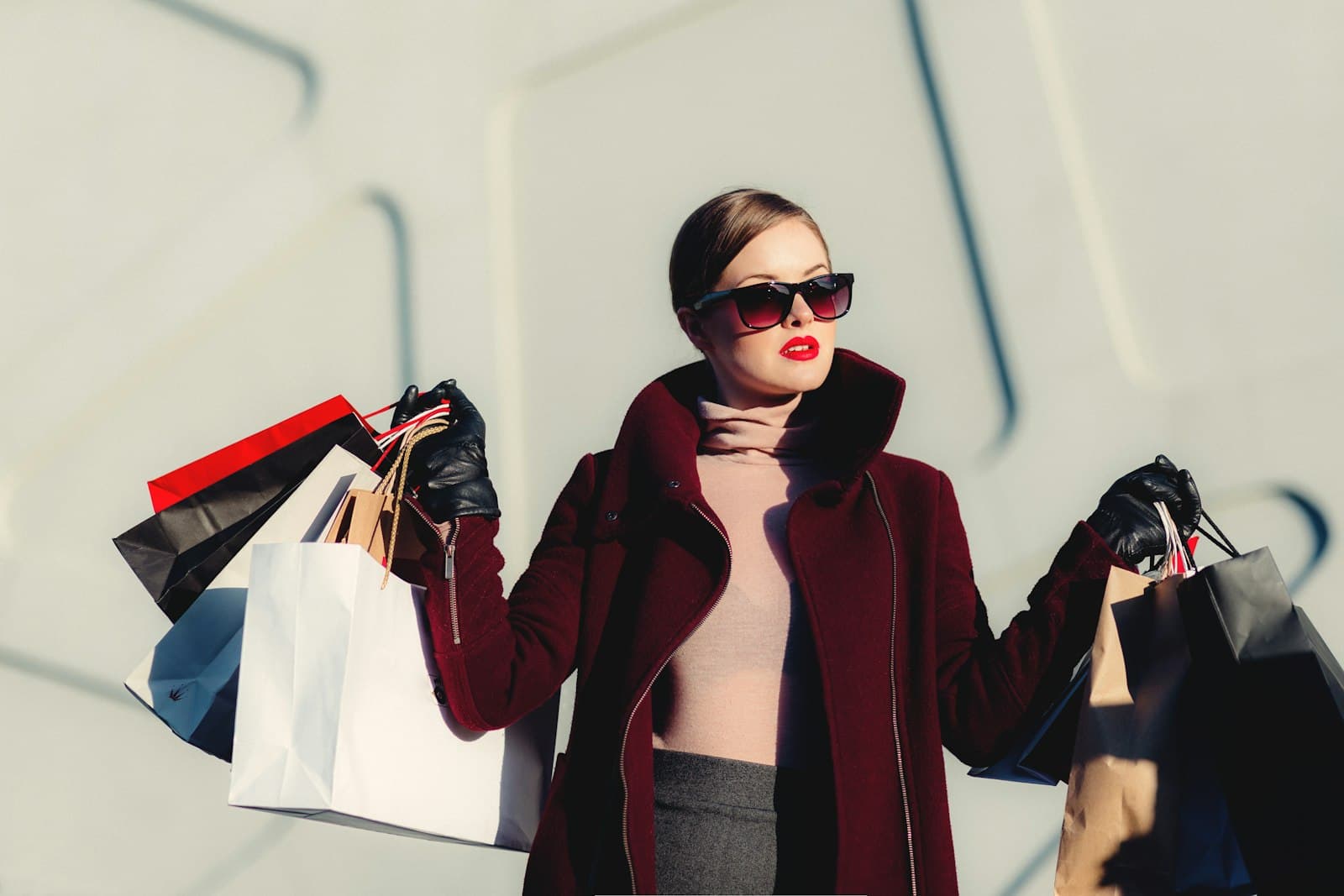 Woman in a burgundy coat and sunglasses carrying shopping bags