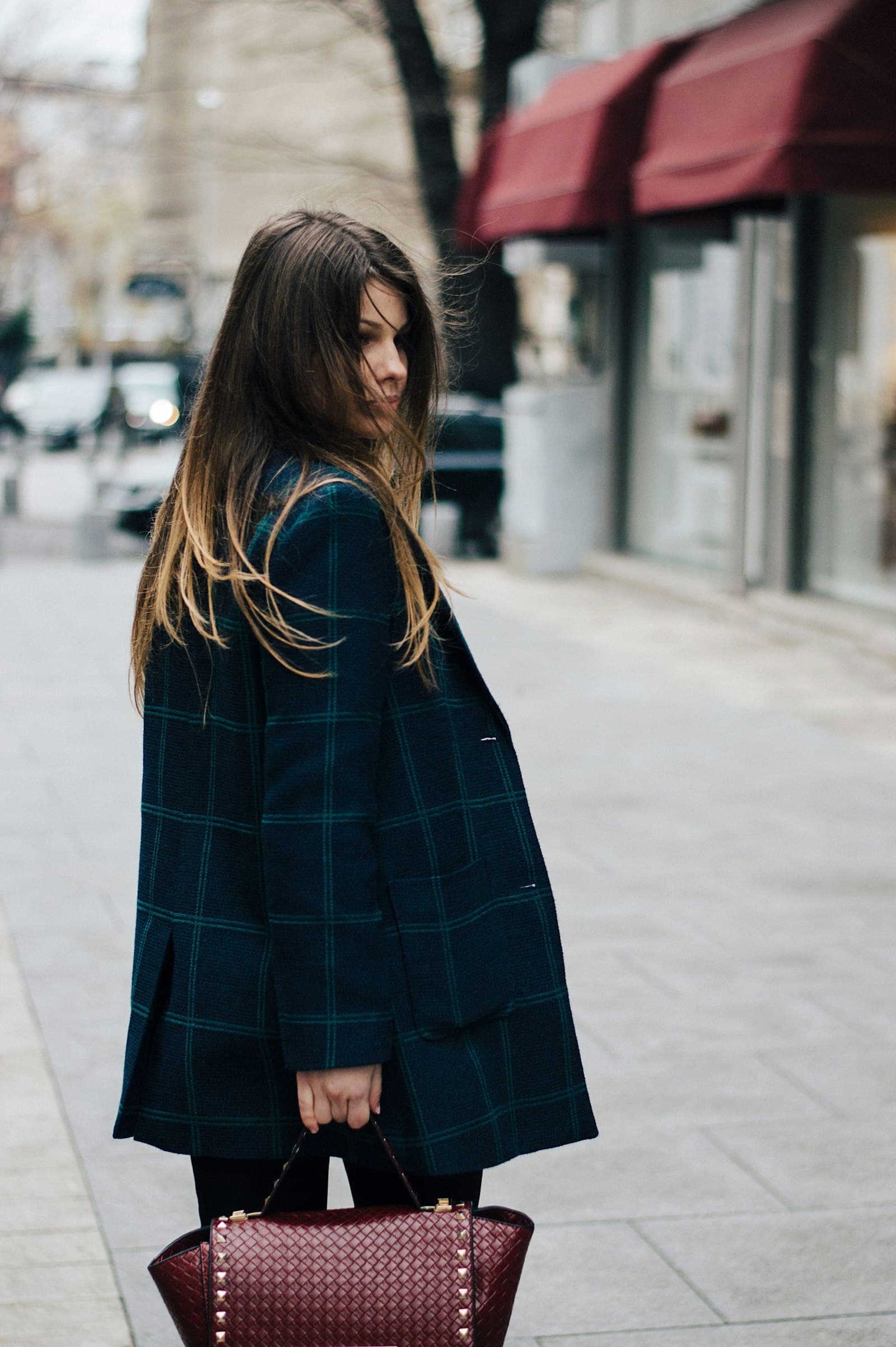 Woman in a long black coat walking on a city sidewalk