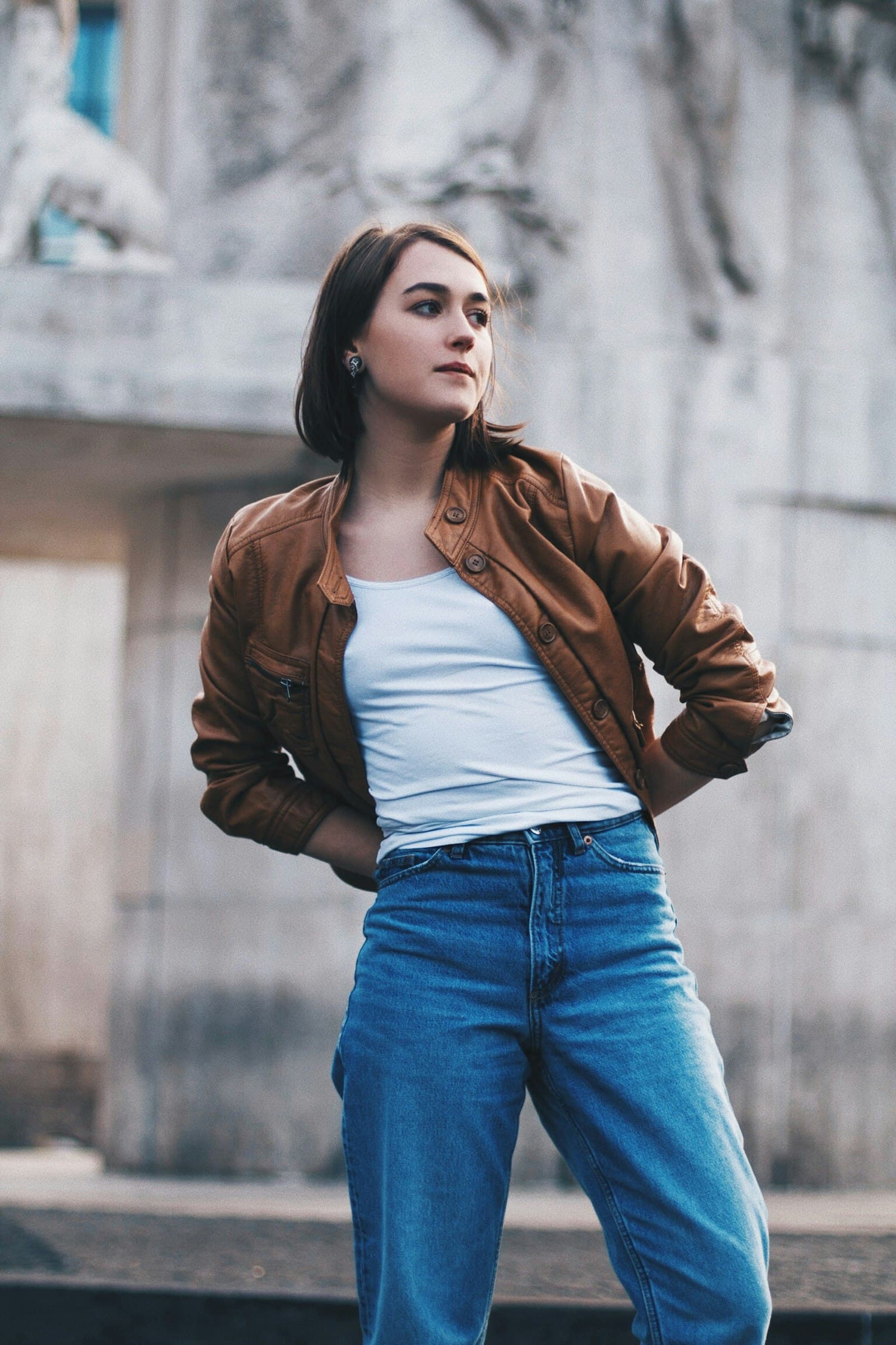 Woman wearing a brown leather jacket with blue jeans on a city street