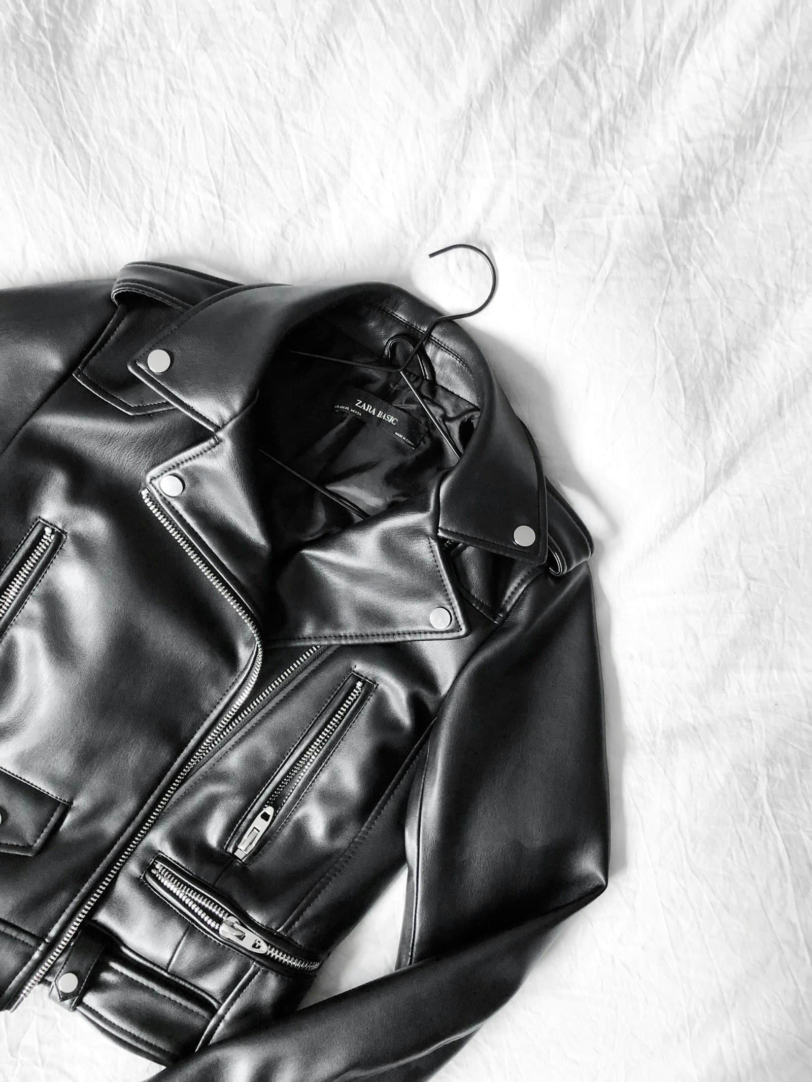 Black leather bomber jacket photographed against a white wall