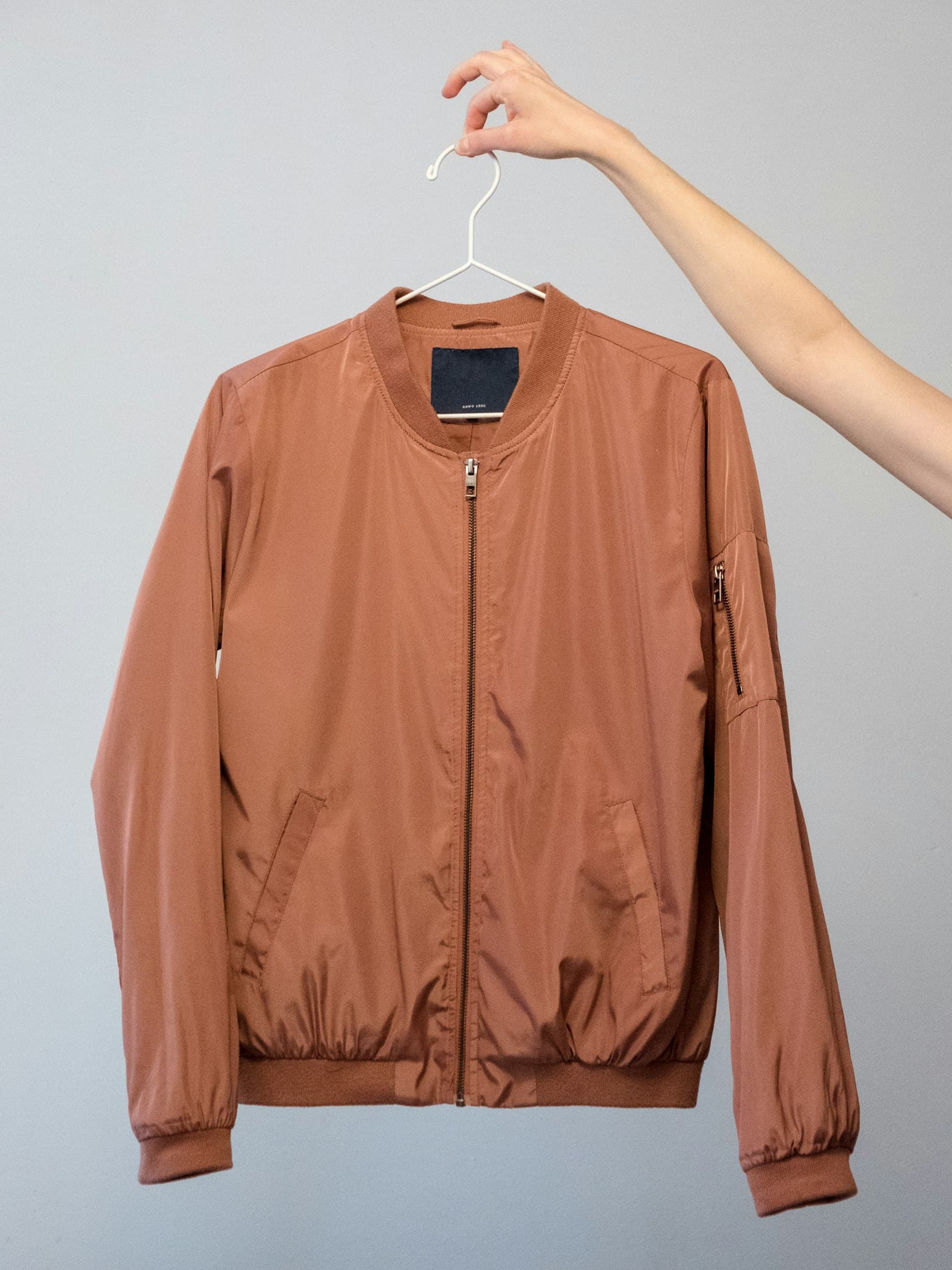 Brown leather bomber jacket held up on a wooden hanger